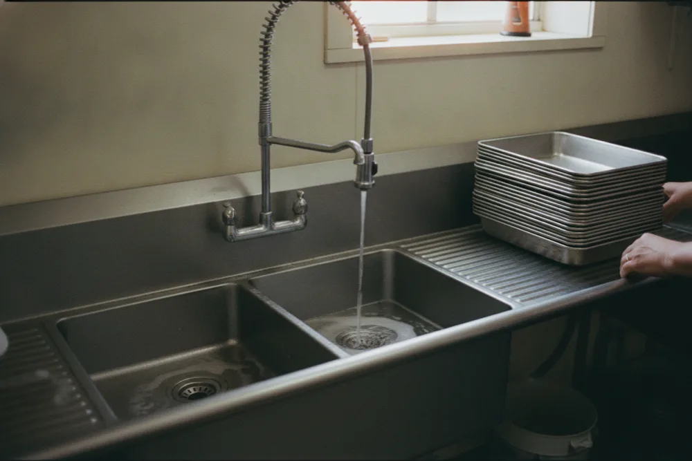 Rinse water swirling down the drain of a three-compartment commercial sink