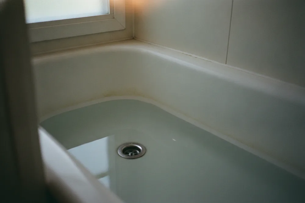 Grey water standing around the open drain of a white bathtub, the classic slow-drain warning sign